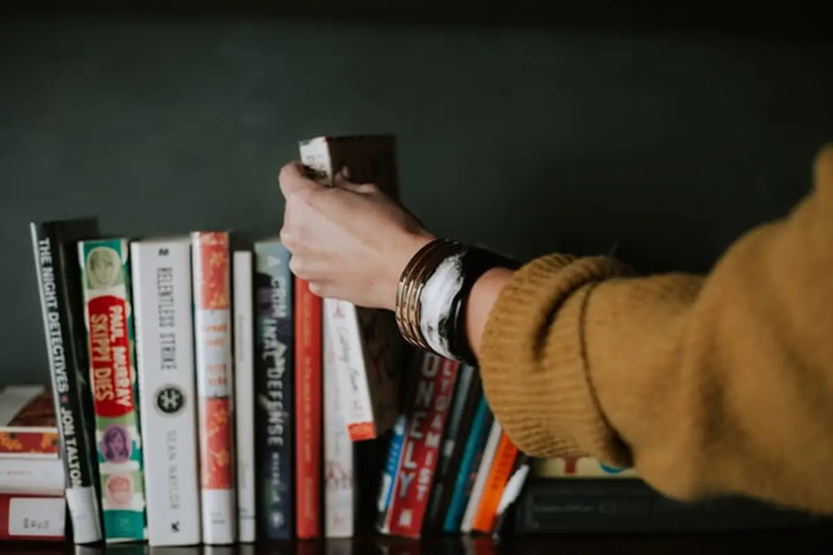 A woman's hand reaching to grab a book on a bookshelf.